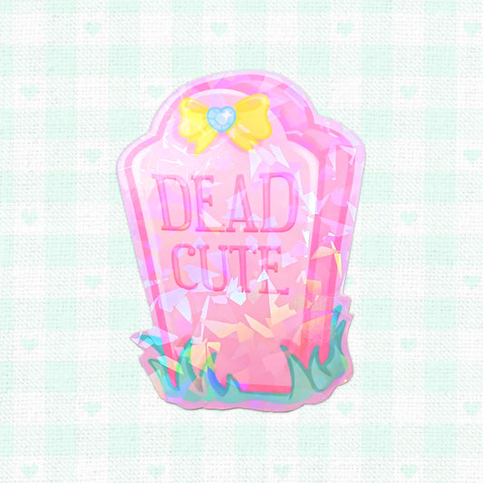 Holographic vinyl sticker of a pink tombstone labeled 'Dead Cute', decorated with playful designs, perfect for adding a unique touch to personal items.