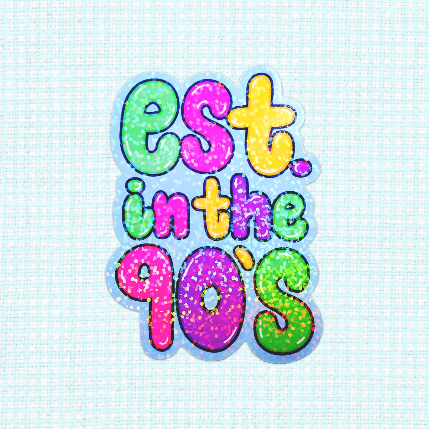 A holographic sticker with colorful text reading "Est. in the 90's," featuring bold, glittery letters.