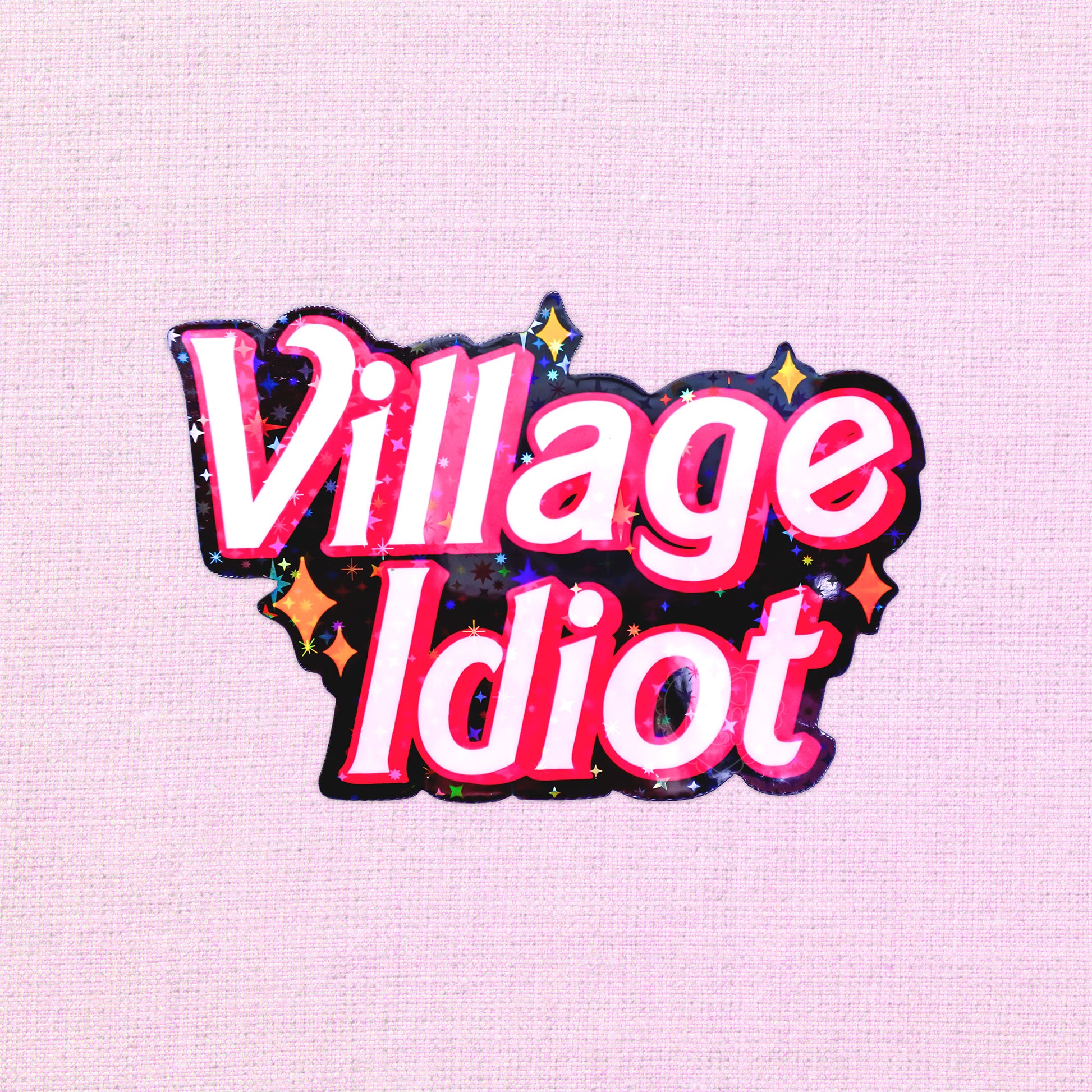 Holographic vinyl sticker with the phrase "Village Idiot" surrounded by stars.